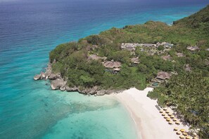 An aerial view of a tropical resort with beachfront villas, clear turquoise waters, and lush greenery.