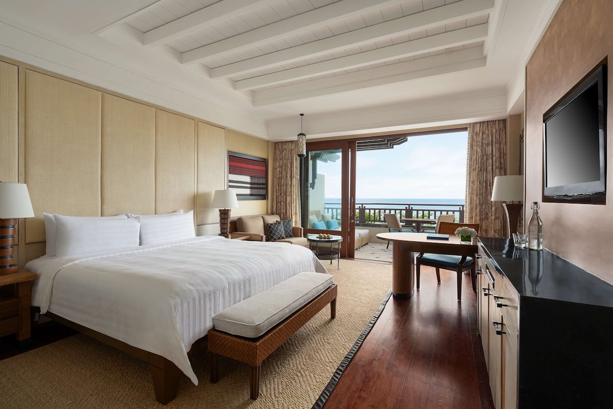 Ein Hotelzimmer mit einem großen Bett, einem Schreibtisch, einem Fernseher und einem Balkon mit Blick.
