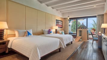 A hotel room with two beds, a desk, a chair, a play area, and a view of the outdoors.