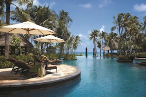 A resort pool area with lounge chairs, umbrellas, and palm trees.