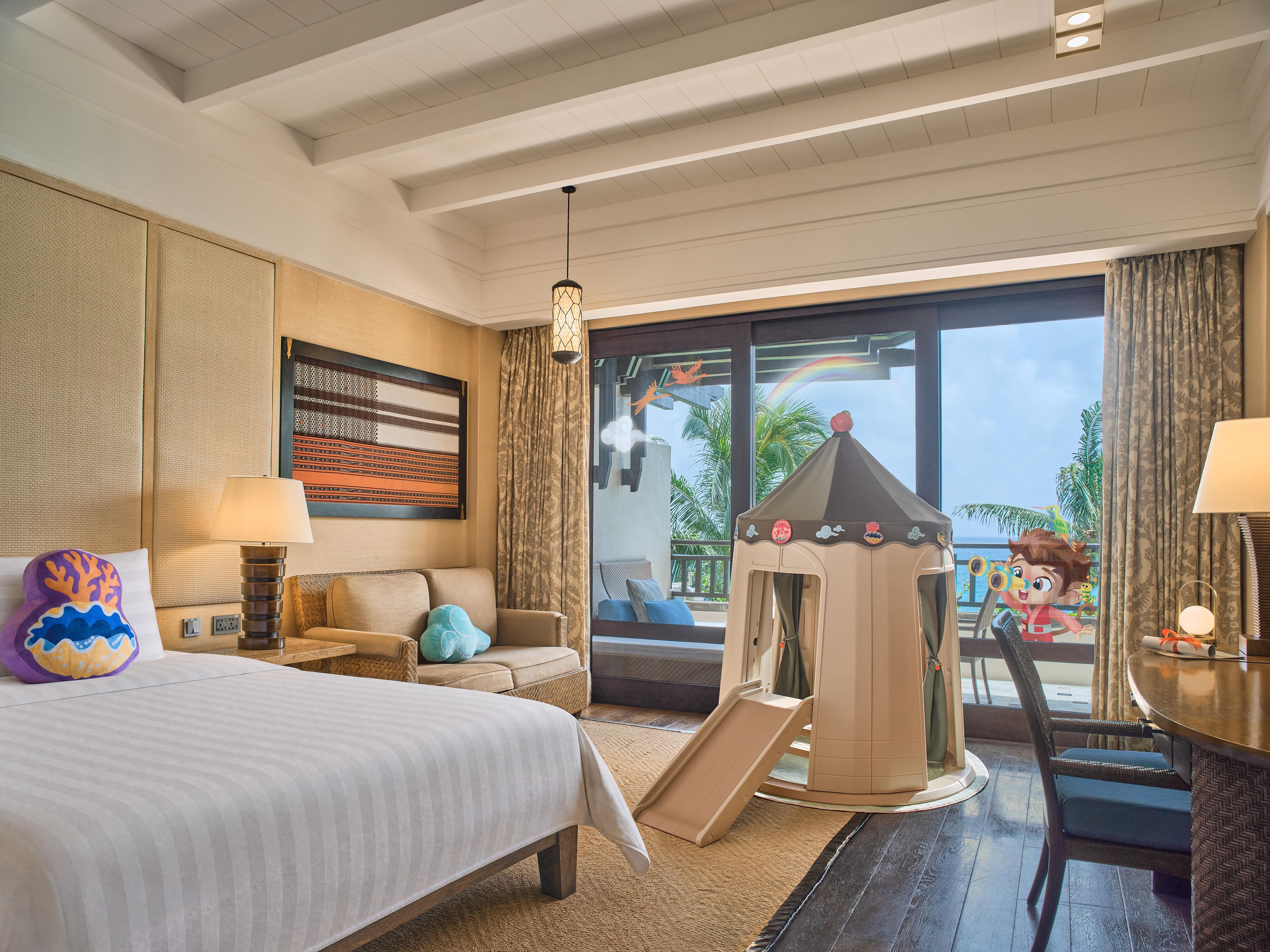 A hotel room with a bed, a play tent, a sofa, and a view of the outdoors.
