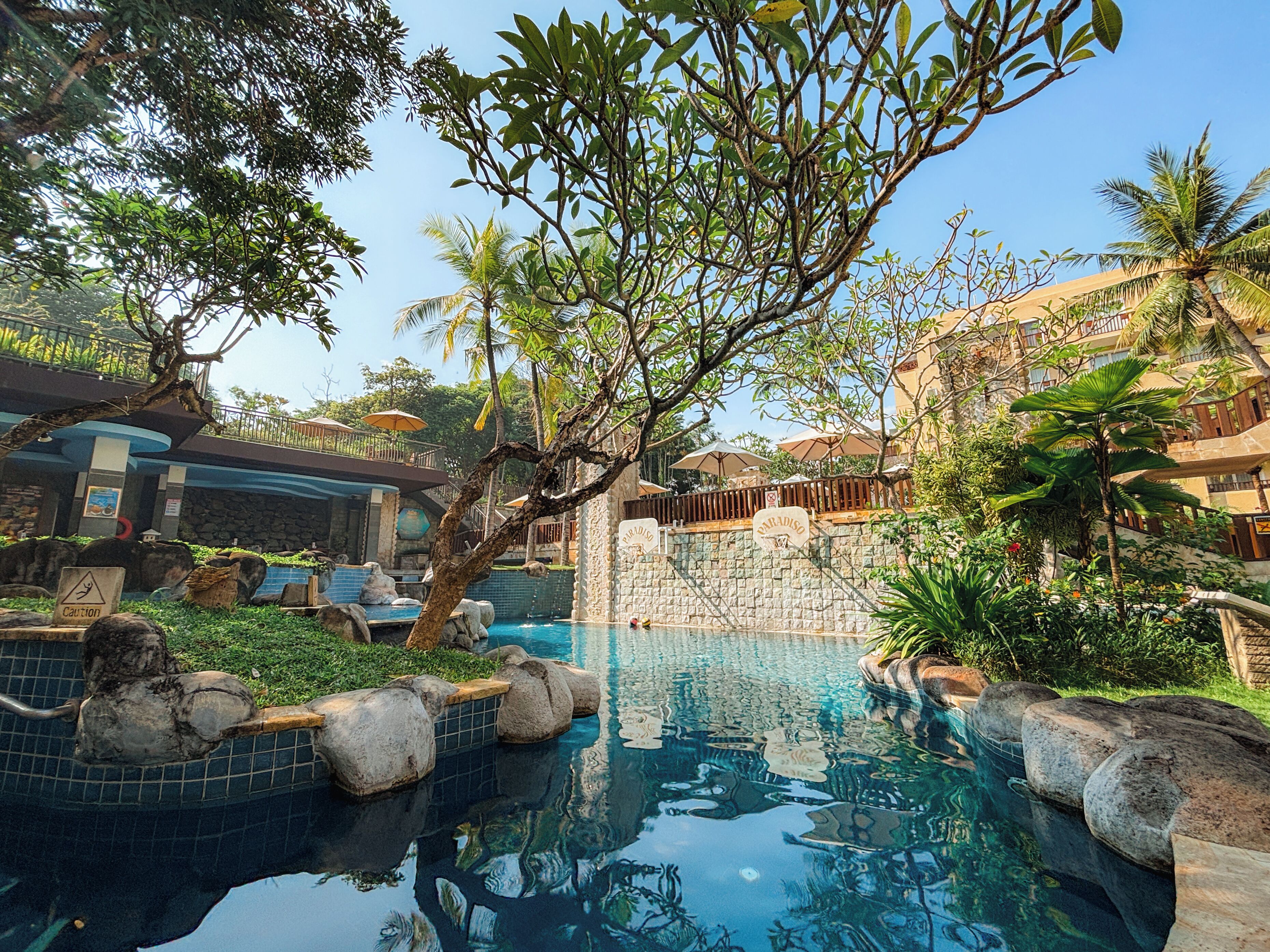 A pool area with clear water, surrounded by rocks and greenery, and a building with a sign that reads "Paradiso".
