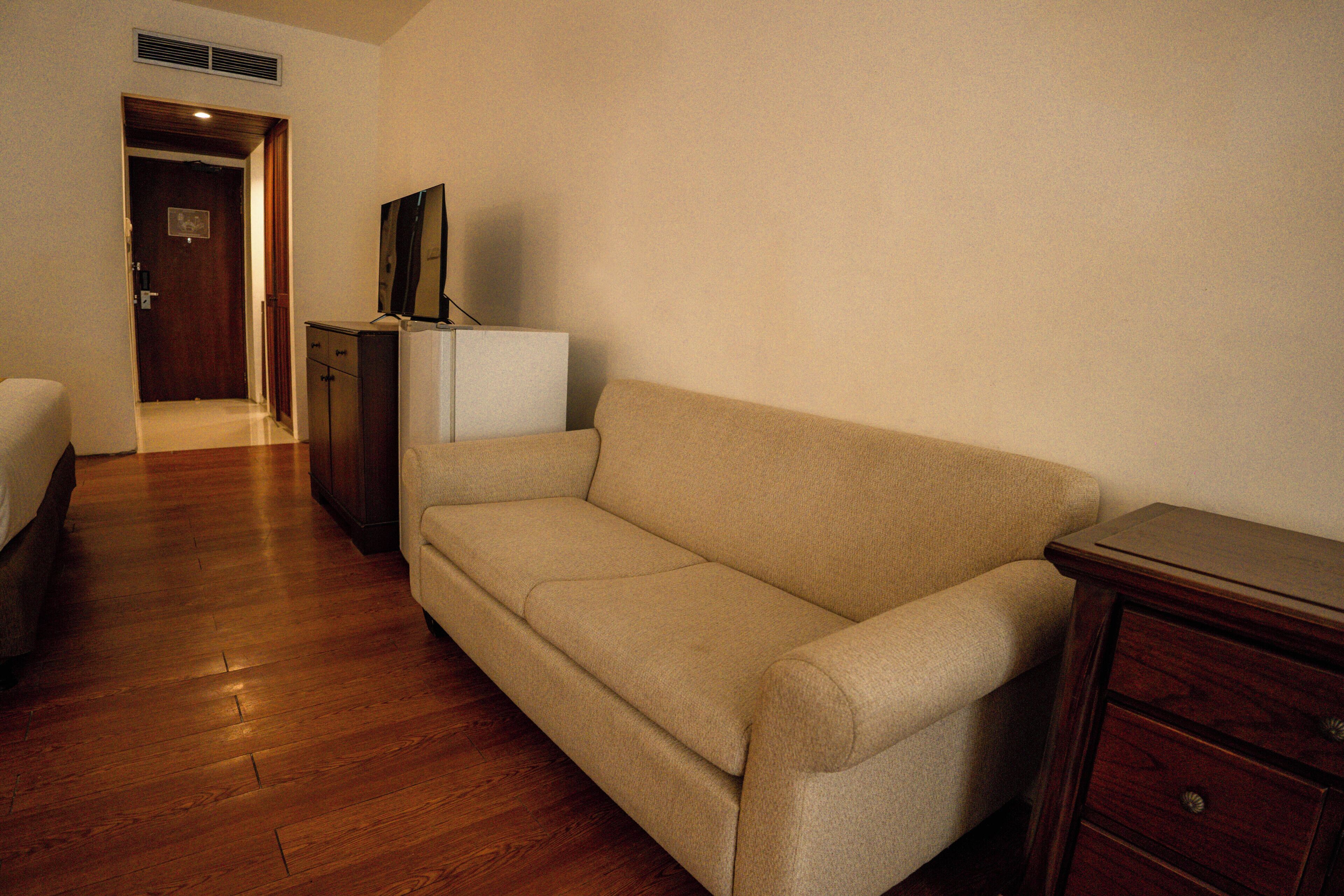 A room with a beige sofa, a wooden dresser, and a small white cabinet.