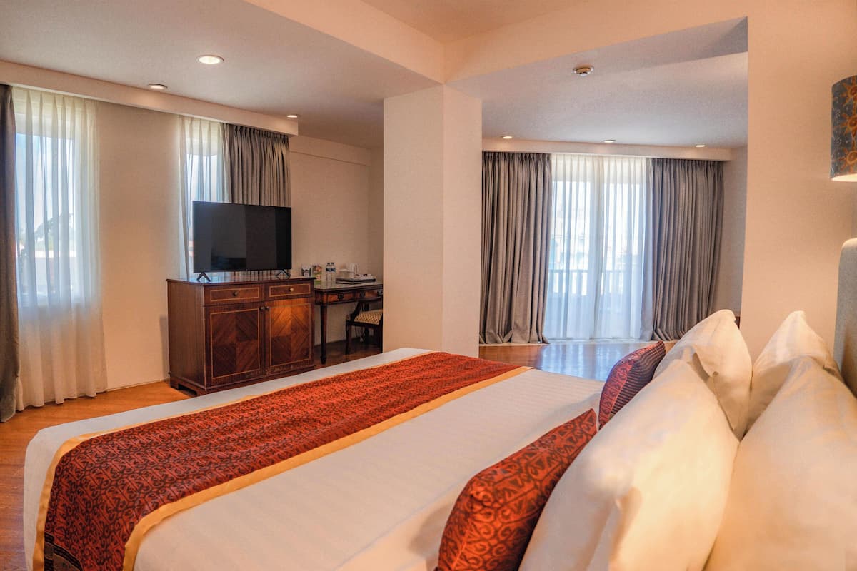 Habitación de hotel con una cama grande, un escritorio y un televisor de pantalla plana, y vistas al exterior a través de las ventanas.