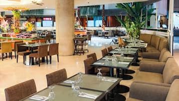 A modern restaurant with glass tables, cushioned seating, and ceiling fans.