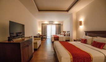 A hotel room with a TV, a desk, a chair, two beds, and a lamp.