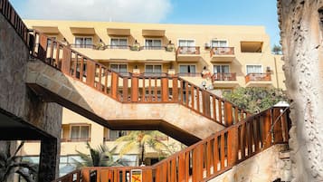 A multi-level hotel with a stone staircase leading to balconies, a pool area, and a clear blue sky.