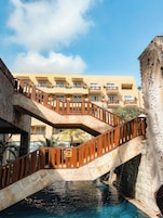 A multi-level hotel with a stone staircase leading to balconies, a pool area, and a clear blue sky.