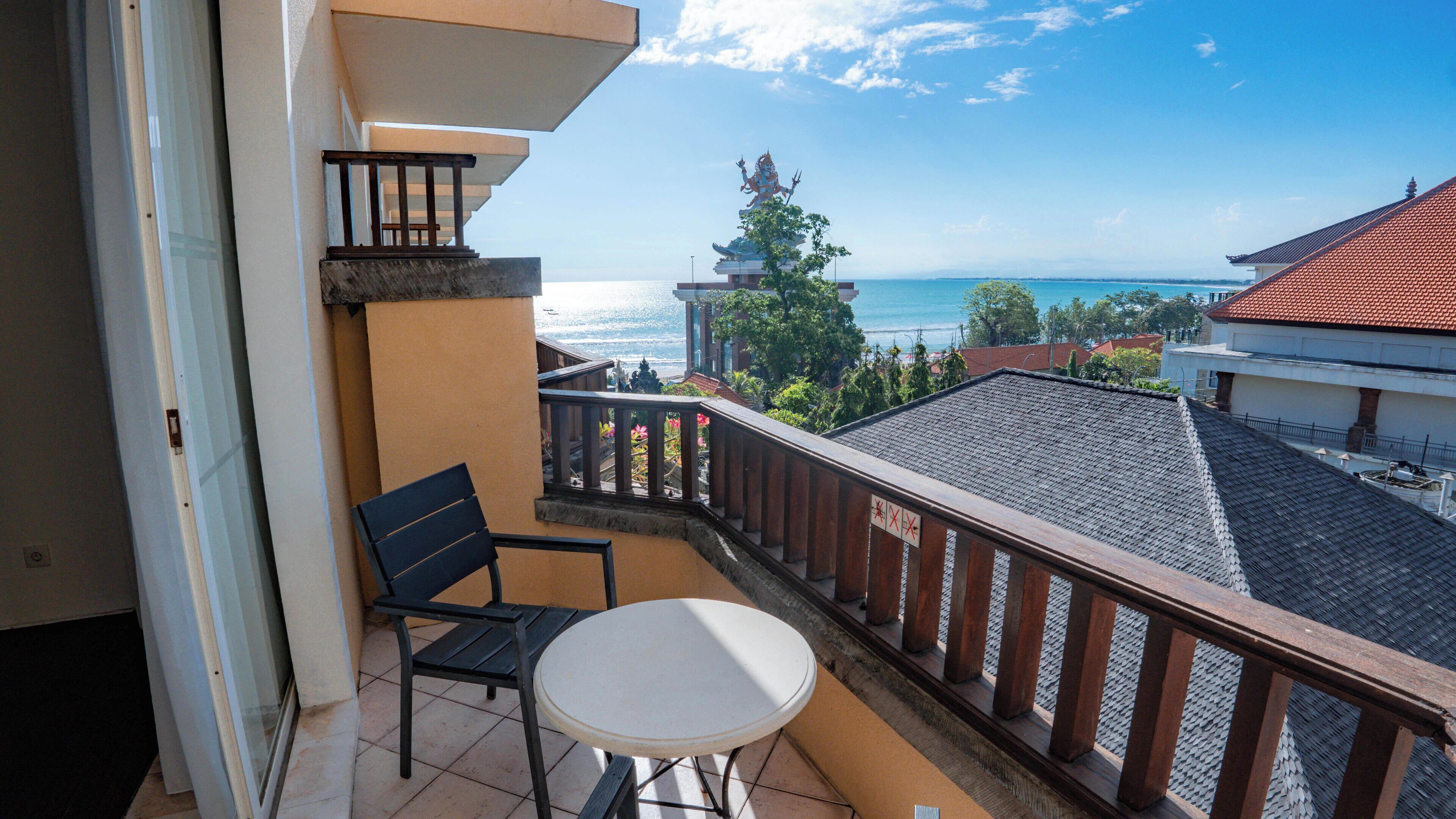 A balcony with a view of the sea, a statue, and a tiled roof.