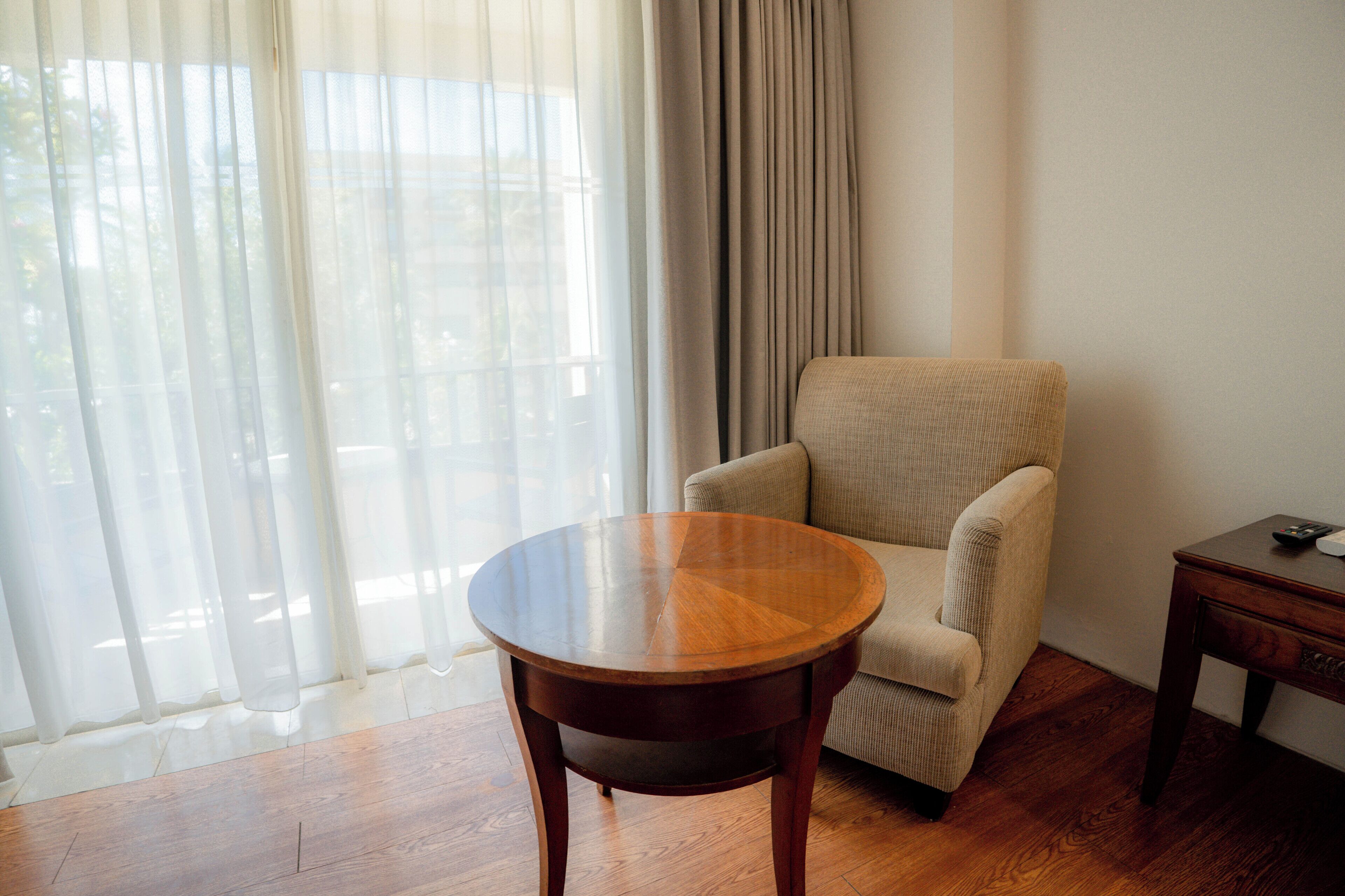 A room with a round wooden table, a beige armchair, and a small wooden side table.