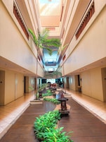 A hotel corridor with a central walkway, potted plants, and a reception area.