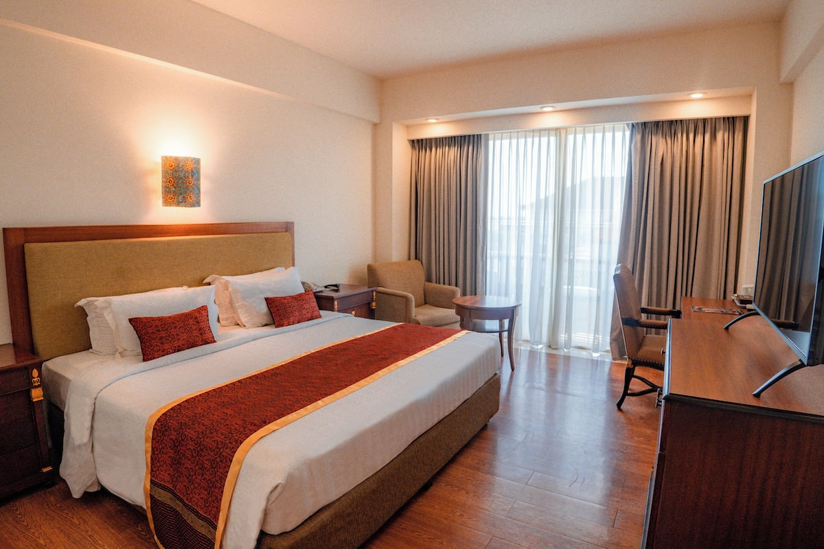 Habitación de hotel con una cama grande, un escritorio, una silla, un televisor y una ventana con cortinas.