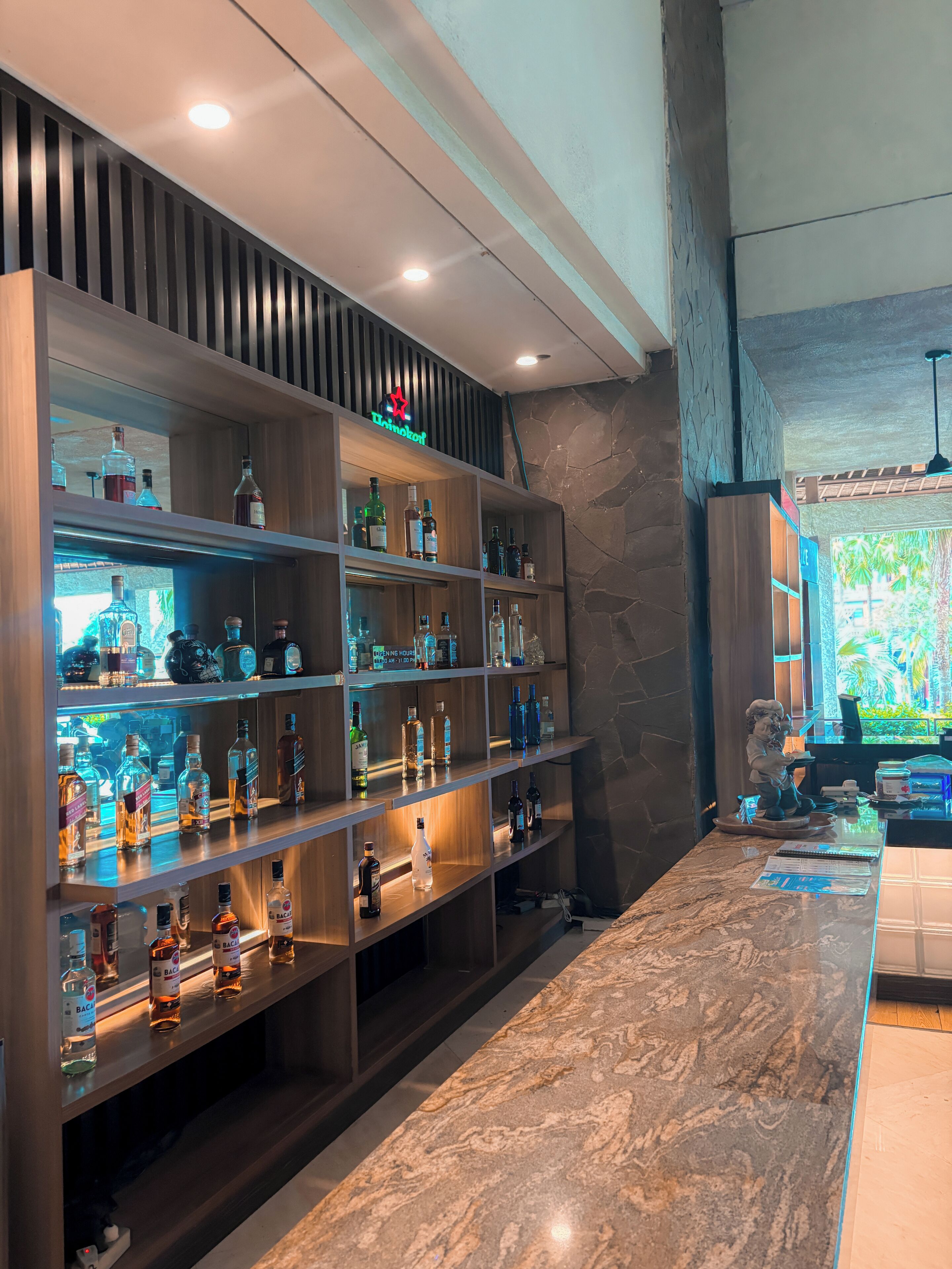 A bar area with shelves of liquor bottles, a marble countertop, and a stone wall.
