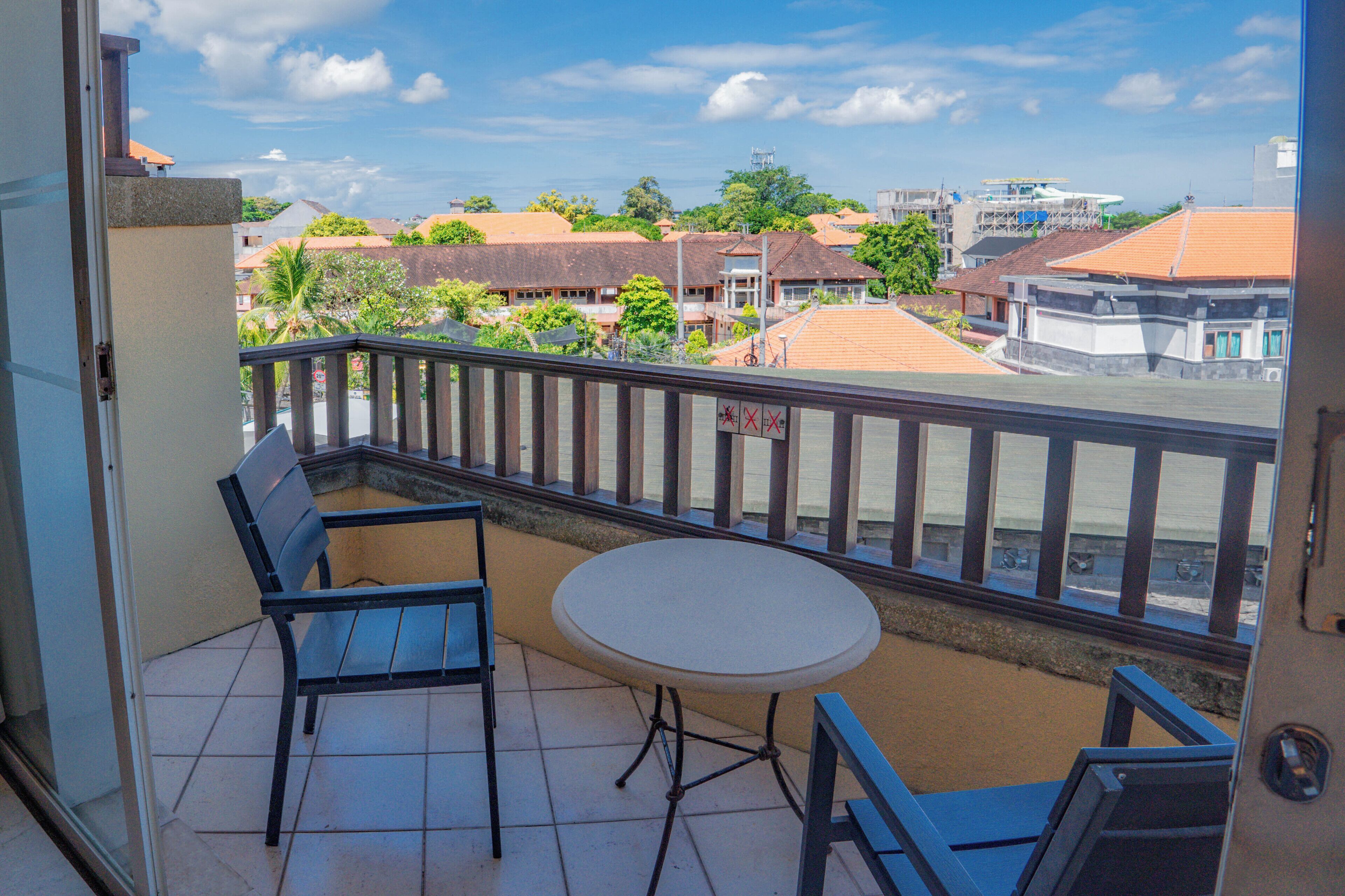 A balcony with a table and two chairs, overlooking a residential area with houses and trees.