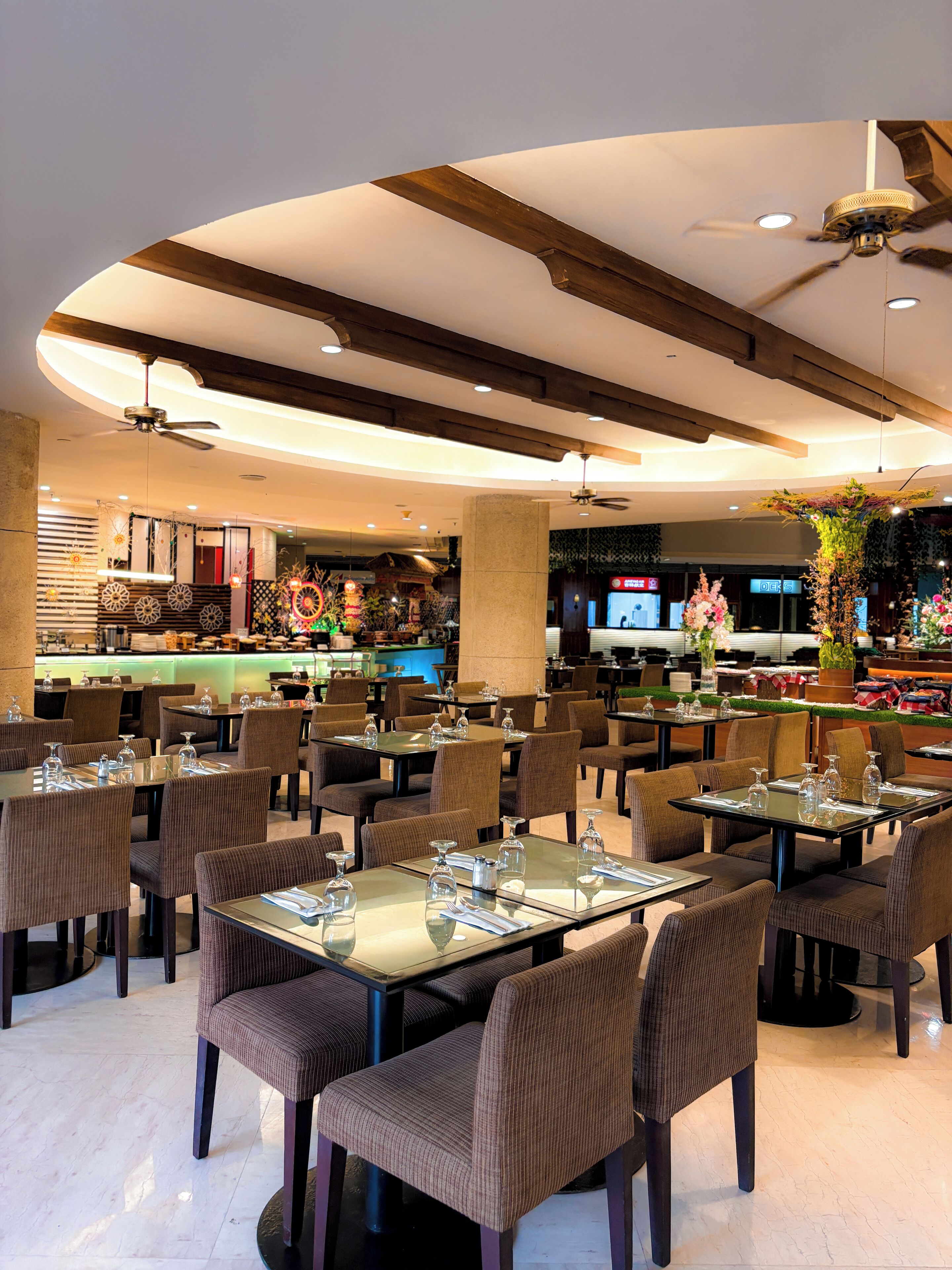 Ein Restaurant mit runden Tischen, braunen Stühlen und einem Deckenventilator.