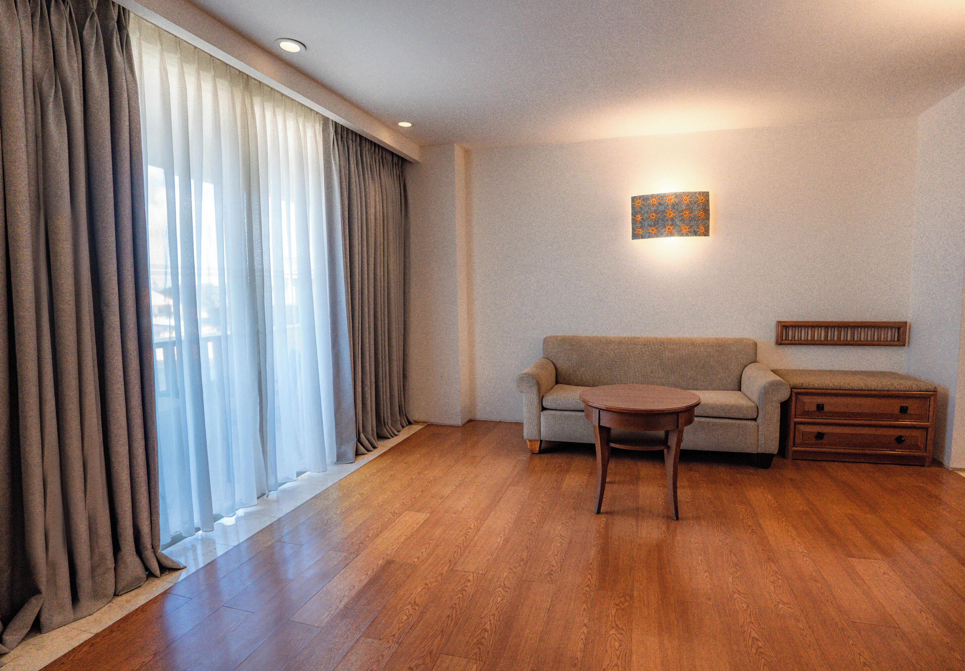 Una habitación con sofá, una mesita, suelo de madera y una ventana con cortinas.