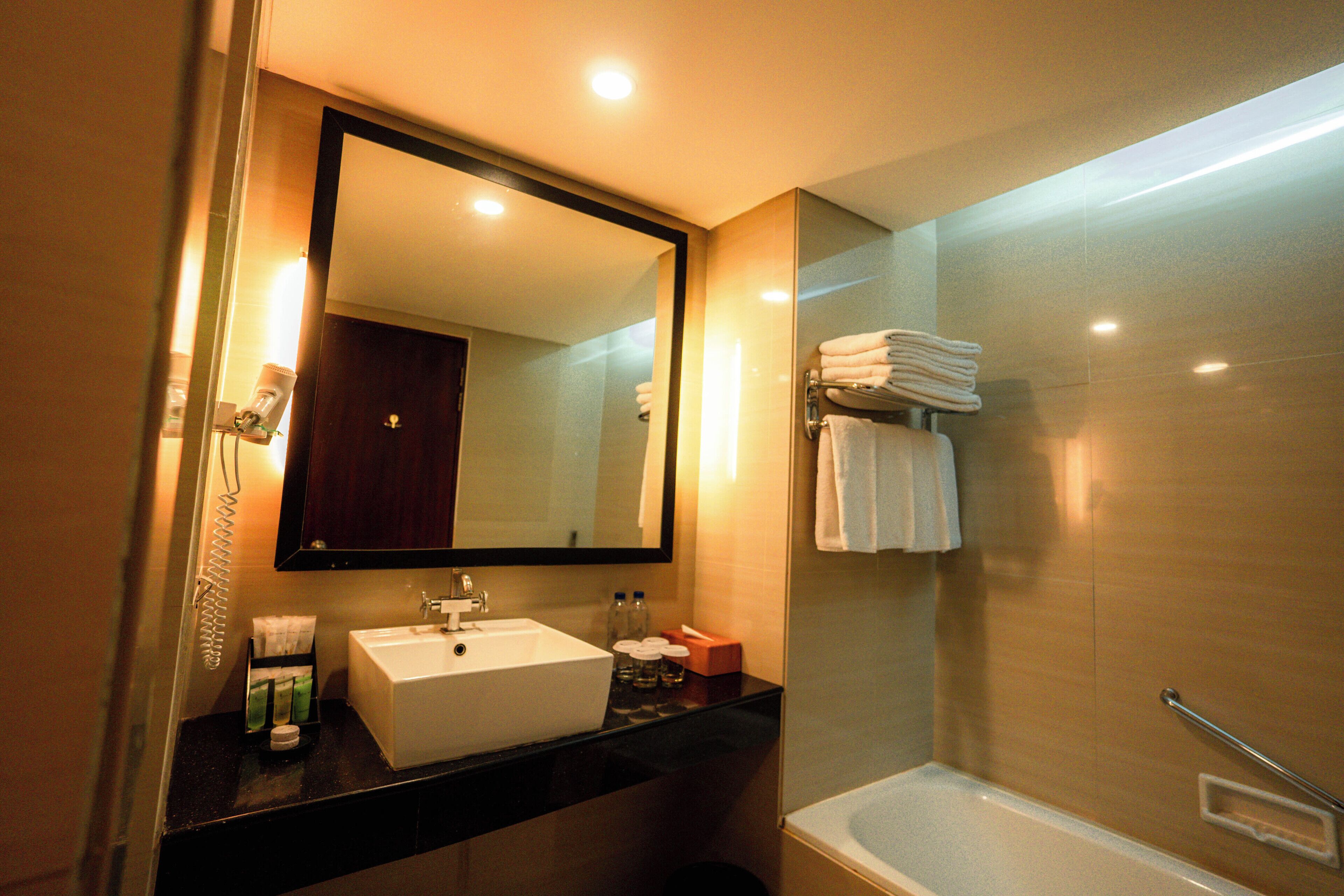 A hotel bathroom with a large mirror, a sink, a bathtub, and a towel rack.