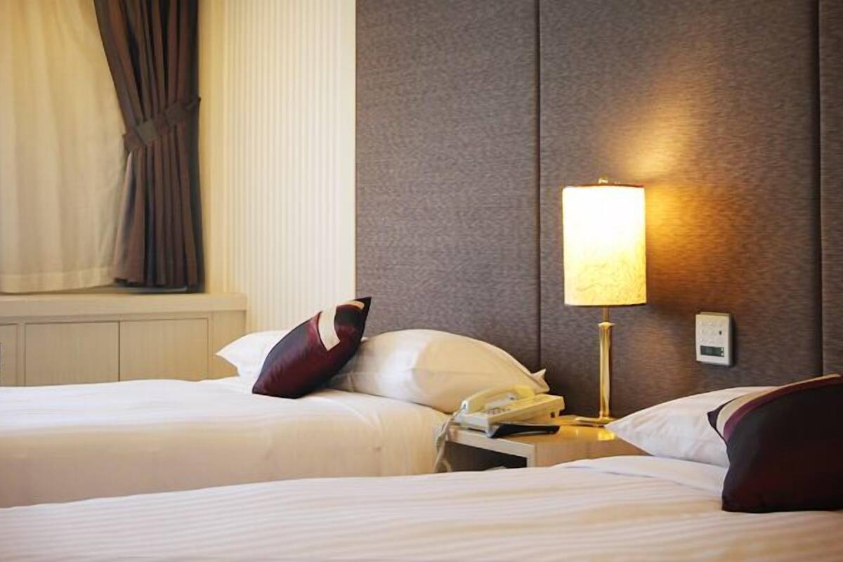 A hotel room with two beds, a bedside lamp, a phone, and a window with curtains.