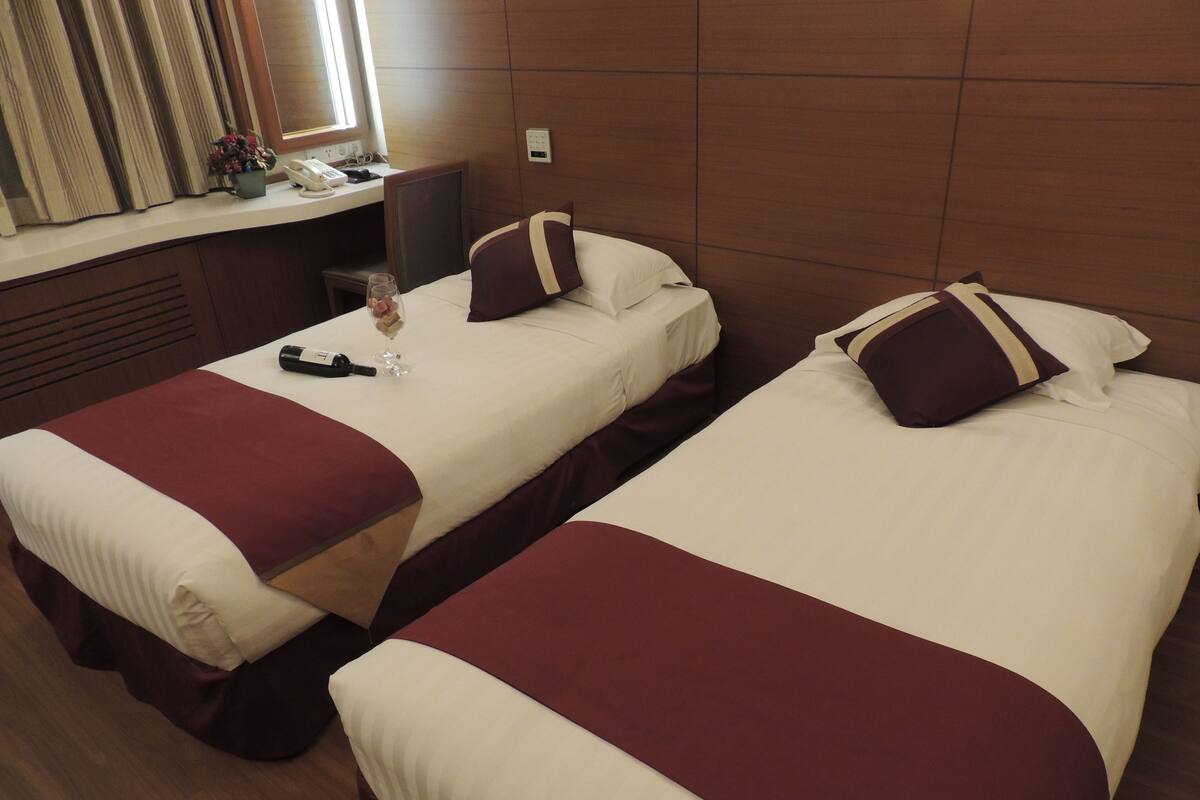 Two single beds with red and white bedding, a bedside table with a lamp, a small potted plant, and a window with curtains.