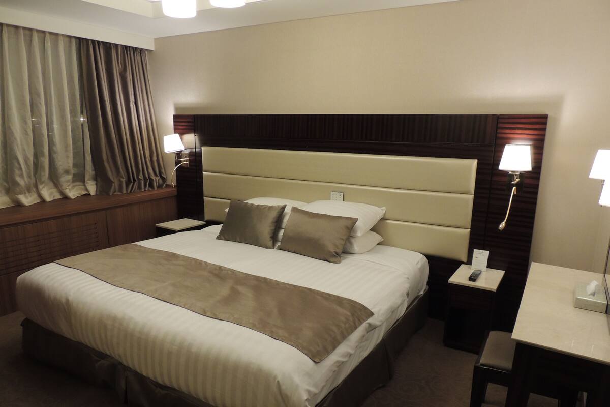 A hotel room with a large bed, two bedside tables, a desk, and a window with curtains.