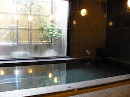 A traditional Japanese-style room with a tatami mat floor, a shoji screen, and a small onsen (hot spring) area.