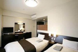 A hotel room with two beds, a desk with a TV, a mirror, and a wall-mounted light fixture.