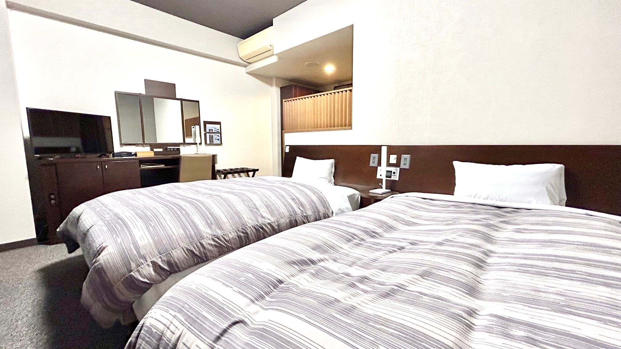 A hotel room with two beds, a desk, a chair, a television, and a mirror.
