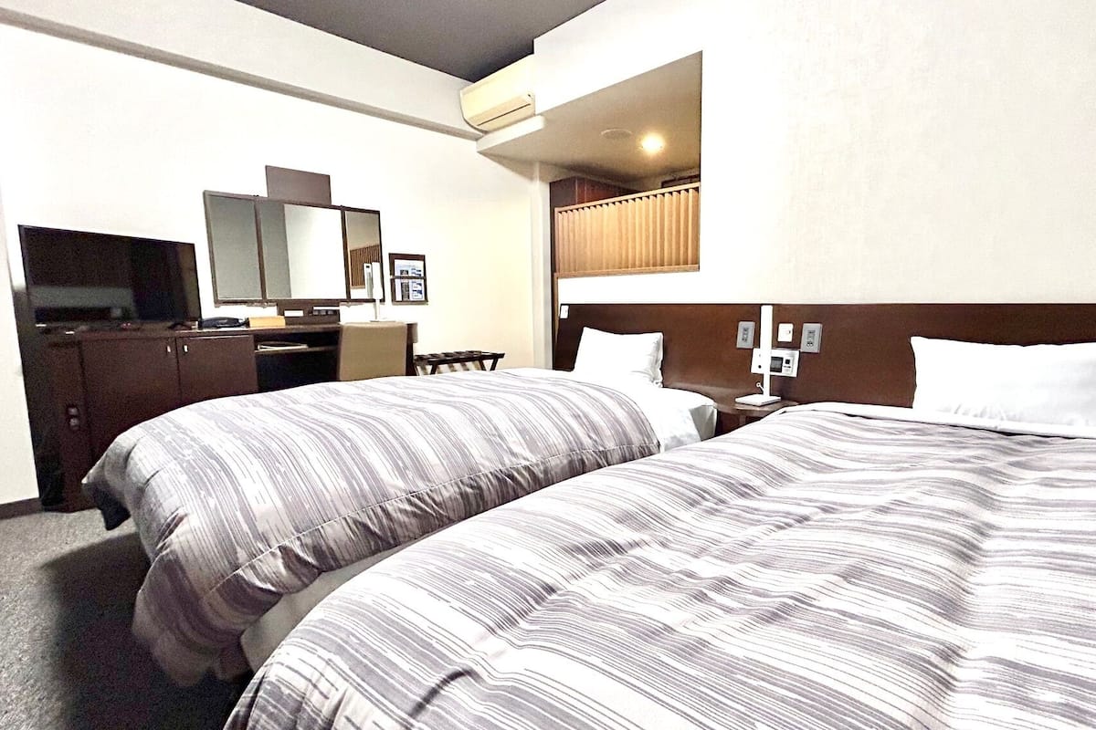 A hotel room with two beds, a desk, a chair, a television, and a mirror.
