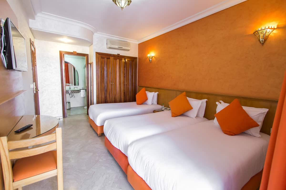 Une chambre d’hôtel avec deux lits, une télévision et une salle de bain visible à travers une porte ouverte.
