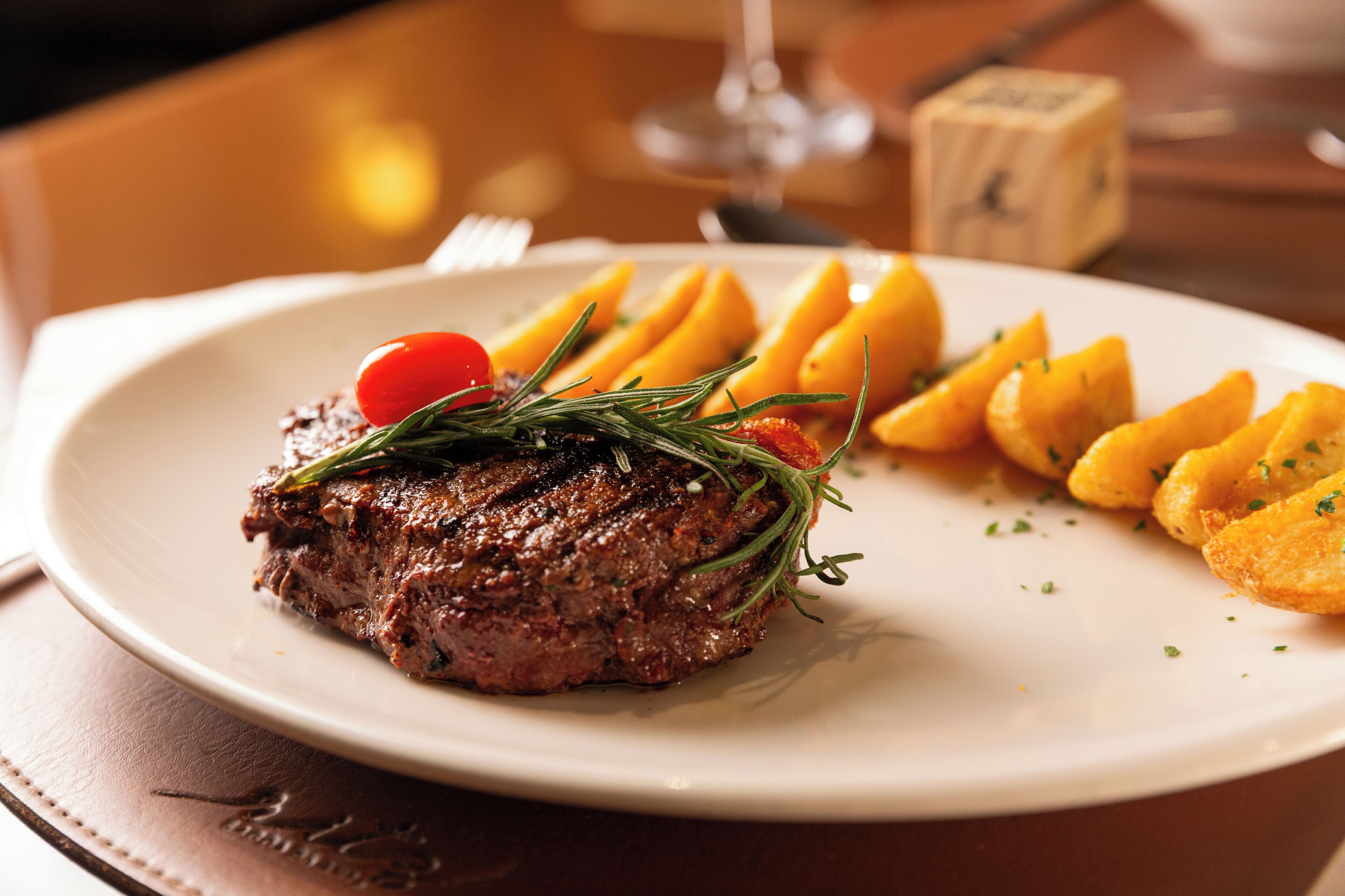 Un plato con un bistec, gajos de limón y un tomate cherry.