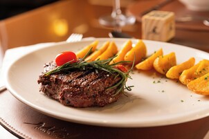 Un plato con un bistec, gajos de limón y un tomate cherry.