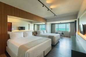 A hotel room with two beds, a TV, a desk, and a view of the sea. - Ritz Lagoa Da Anta (Maceió)