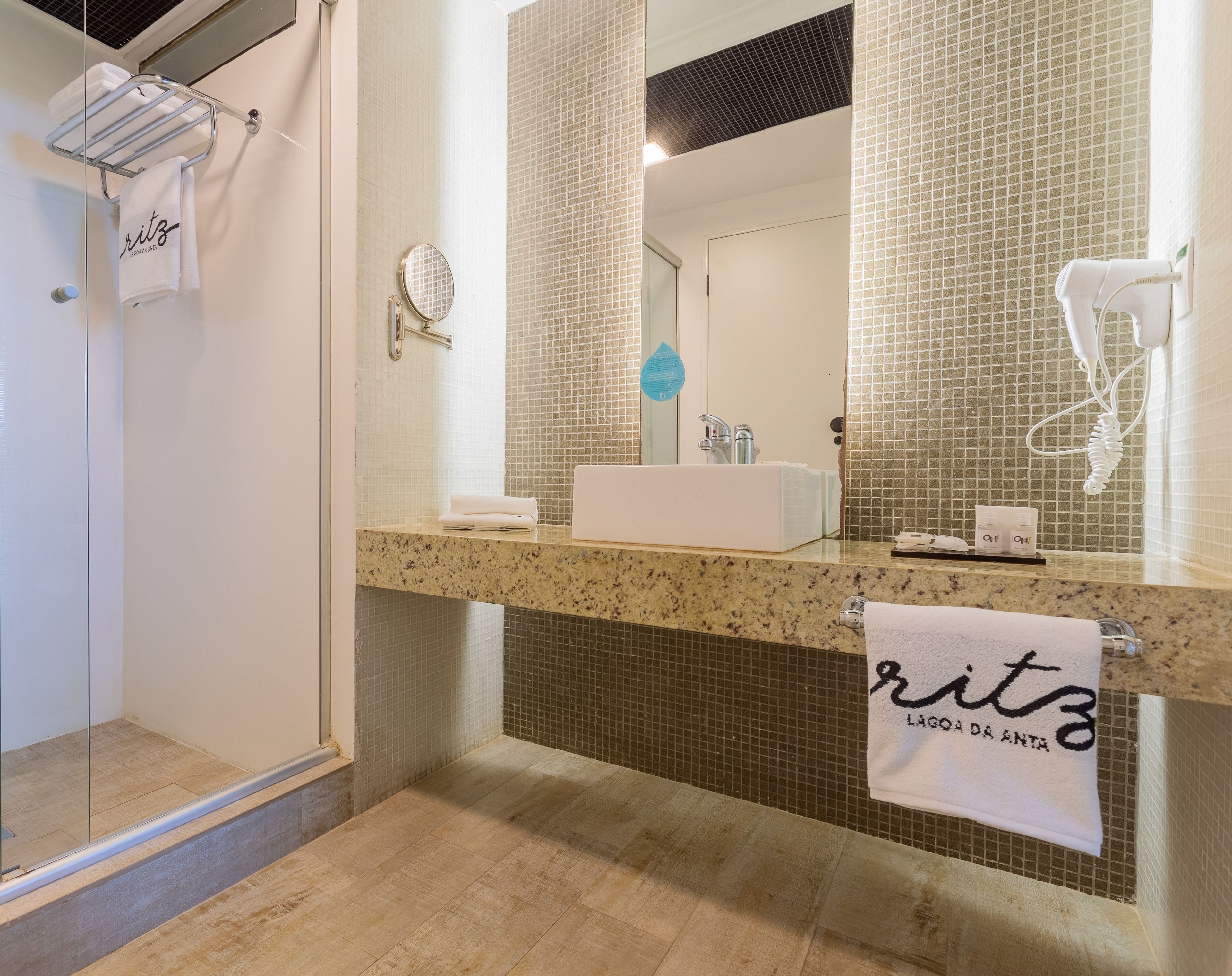 A modern bathroom with a granite countertop, a white sink, a large mirror, and a hairdryer on the wall.