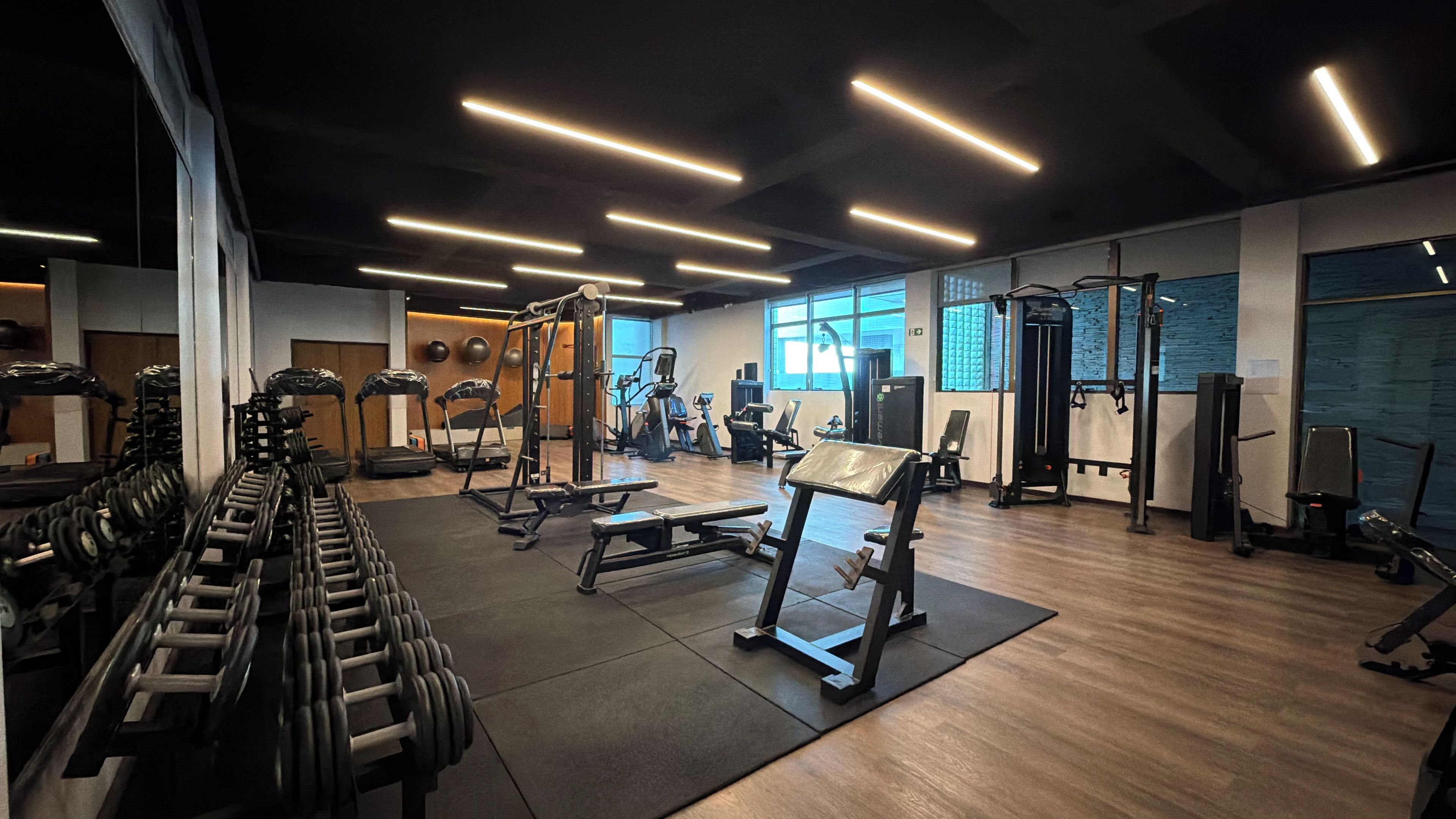 Un gimnasio con diversos equipos de ejercicio, incluyendo cintas de correr, mancuernas y máquinas de pesas.