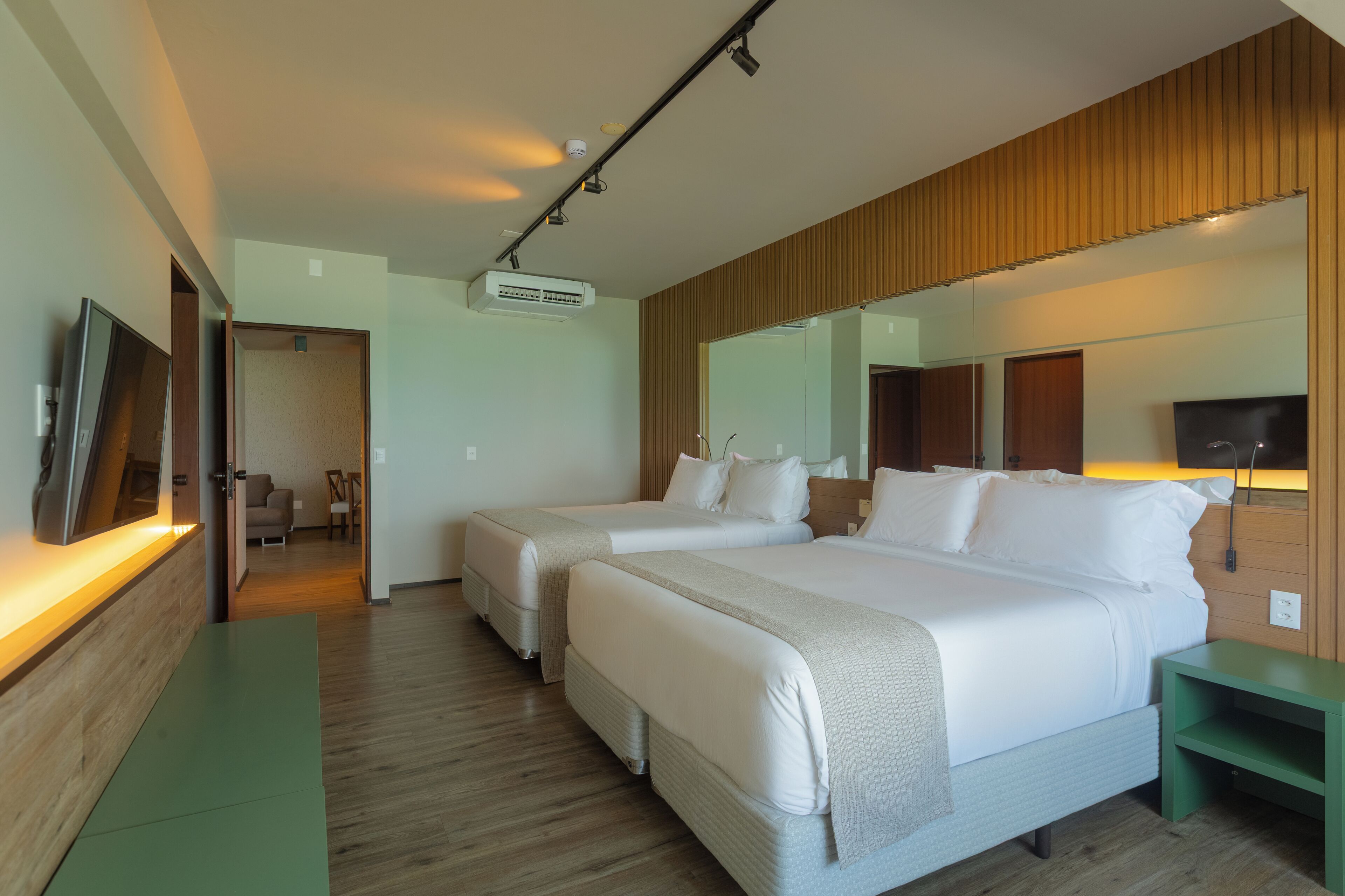 Una habitación de hotel con dos camas, televisión, espejo y pared de paneles de madera.