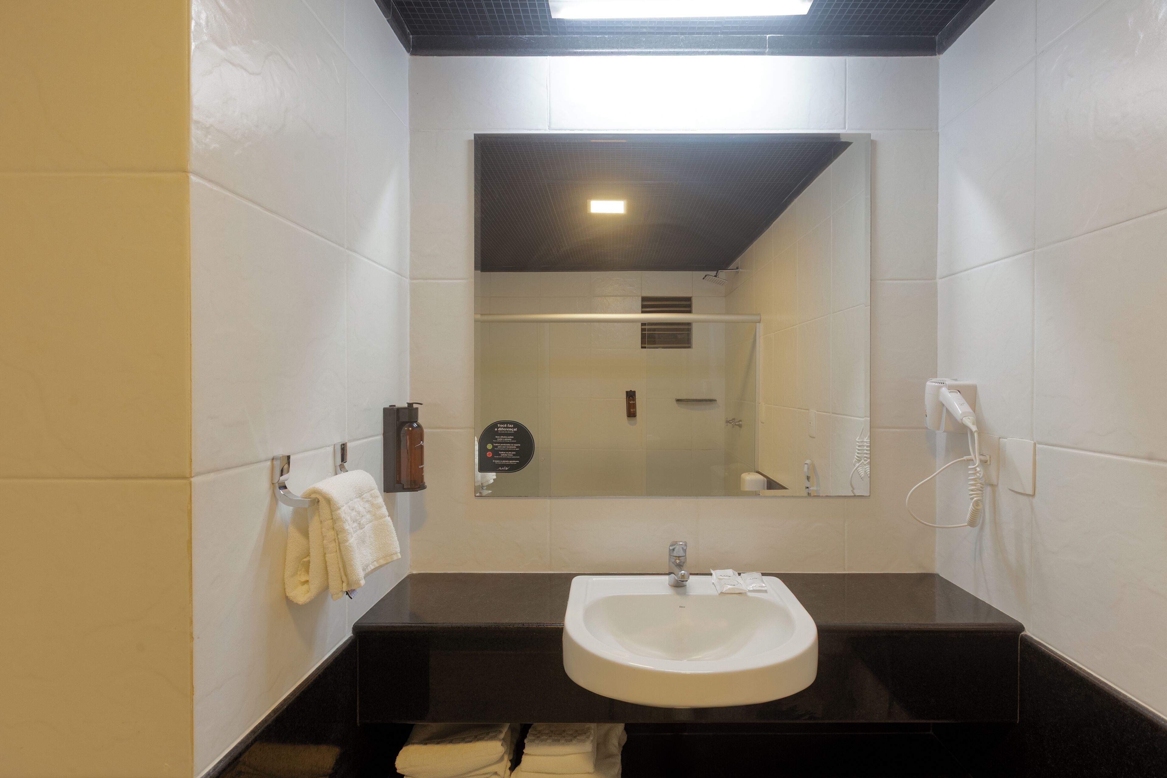 Un baño moderno con un lavamanos blanco, encimera oscura y un espejo sobre el lavamanos.
