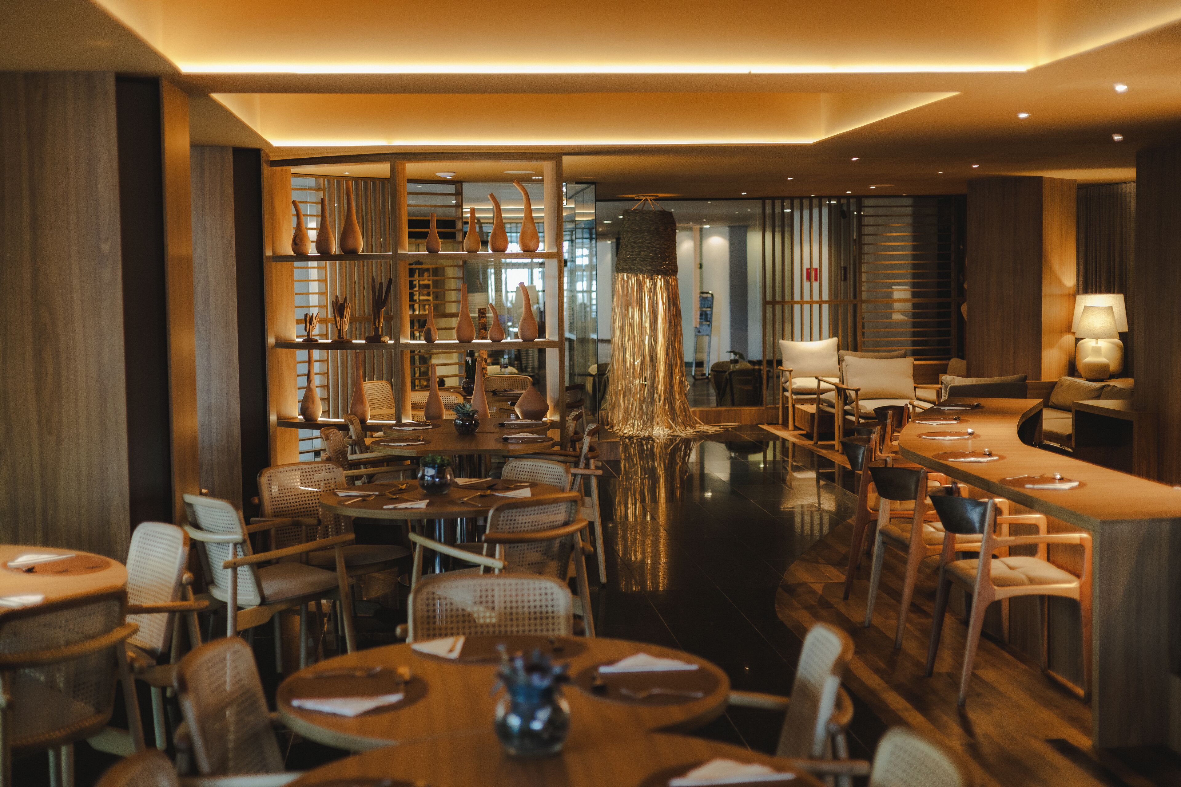 A modern restaurant with wooden furniture, a central bar area, and a decorative water feature.