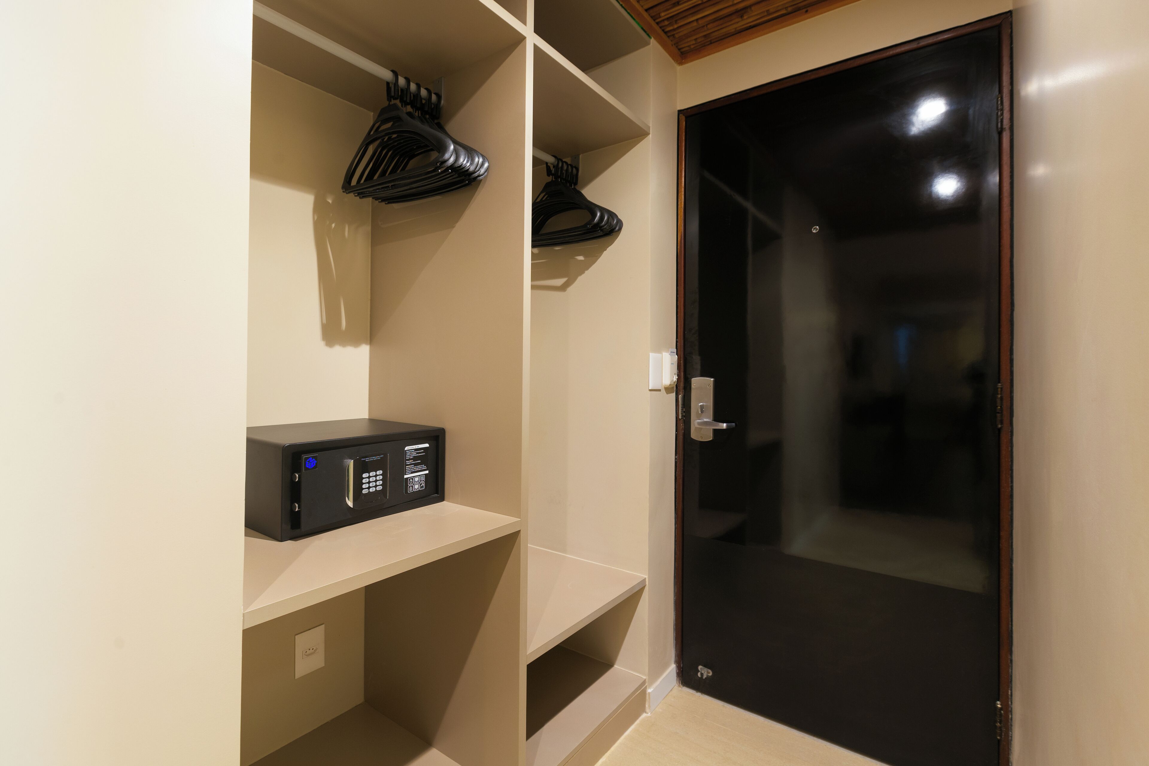 A room with a black door, a black security device on a shelf, and a coat rack.