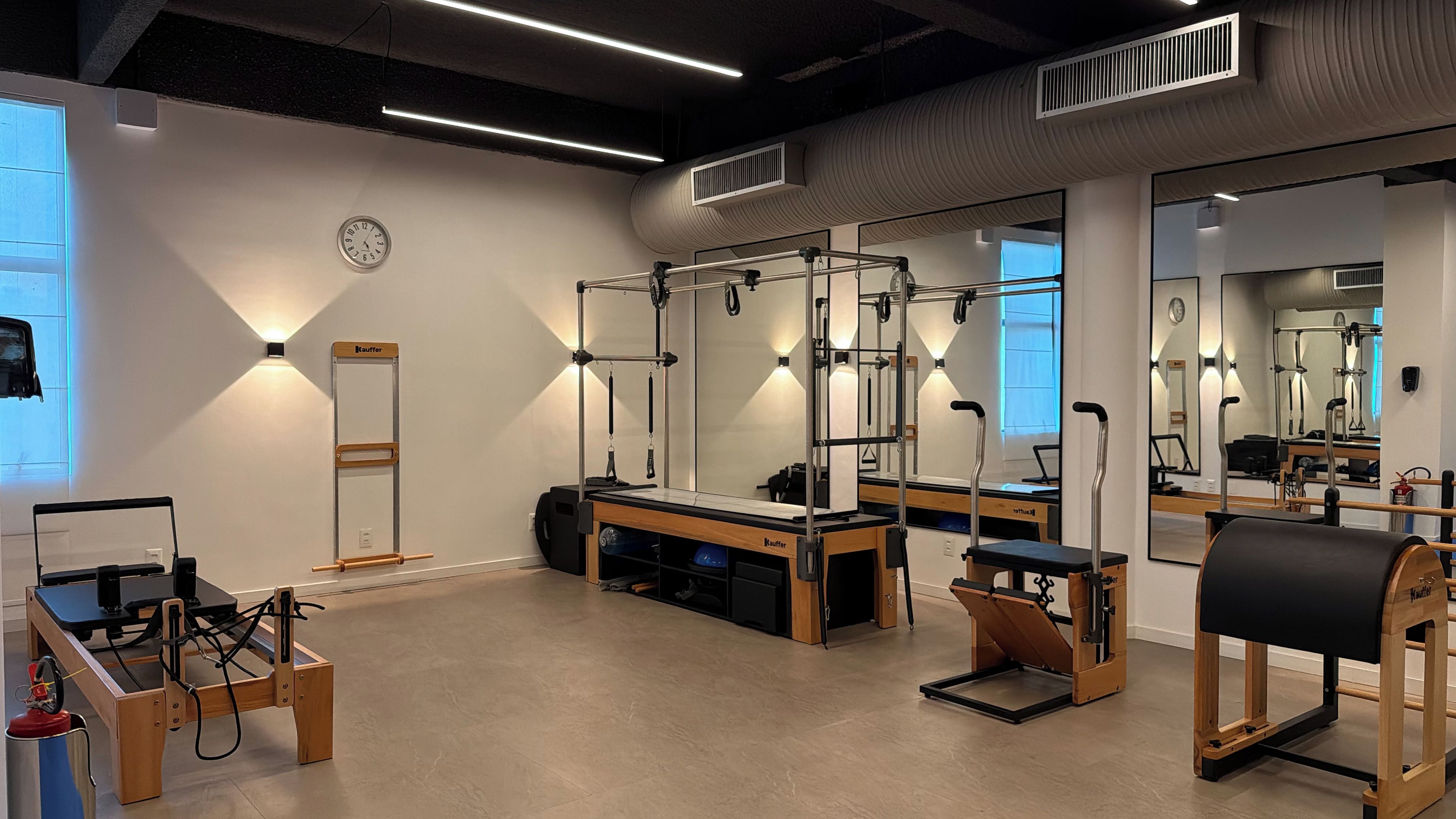 Un estudio de Pilates con equipo, espejos y un reloj en la pared.