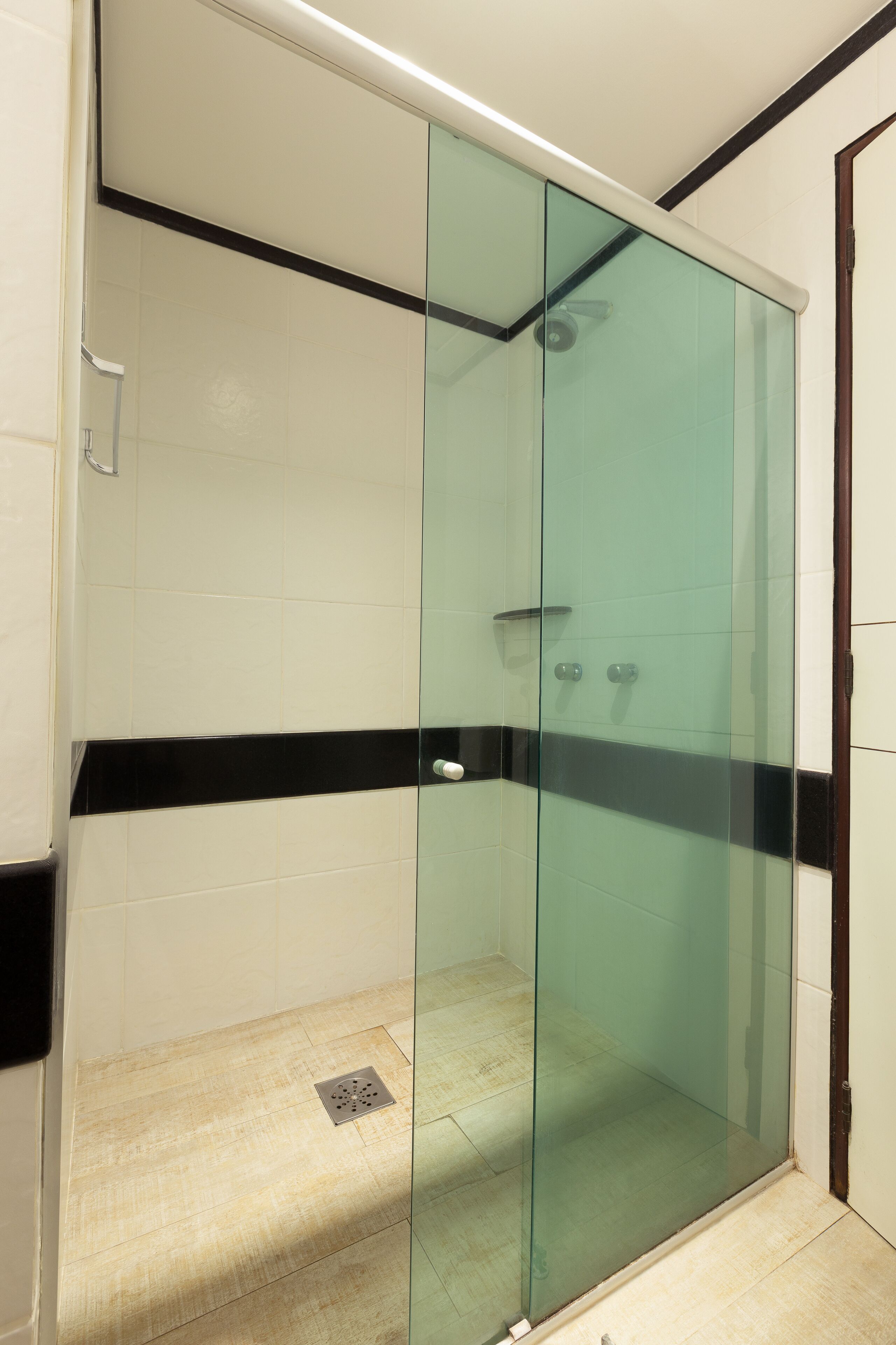 A glass-enclosed shower stall with a black and white tiled floor and a visible drain.