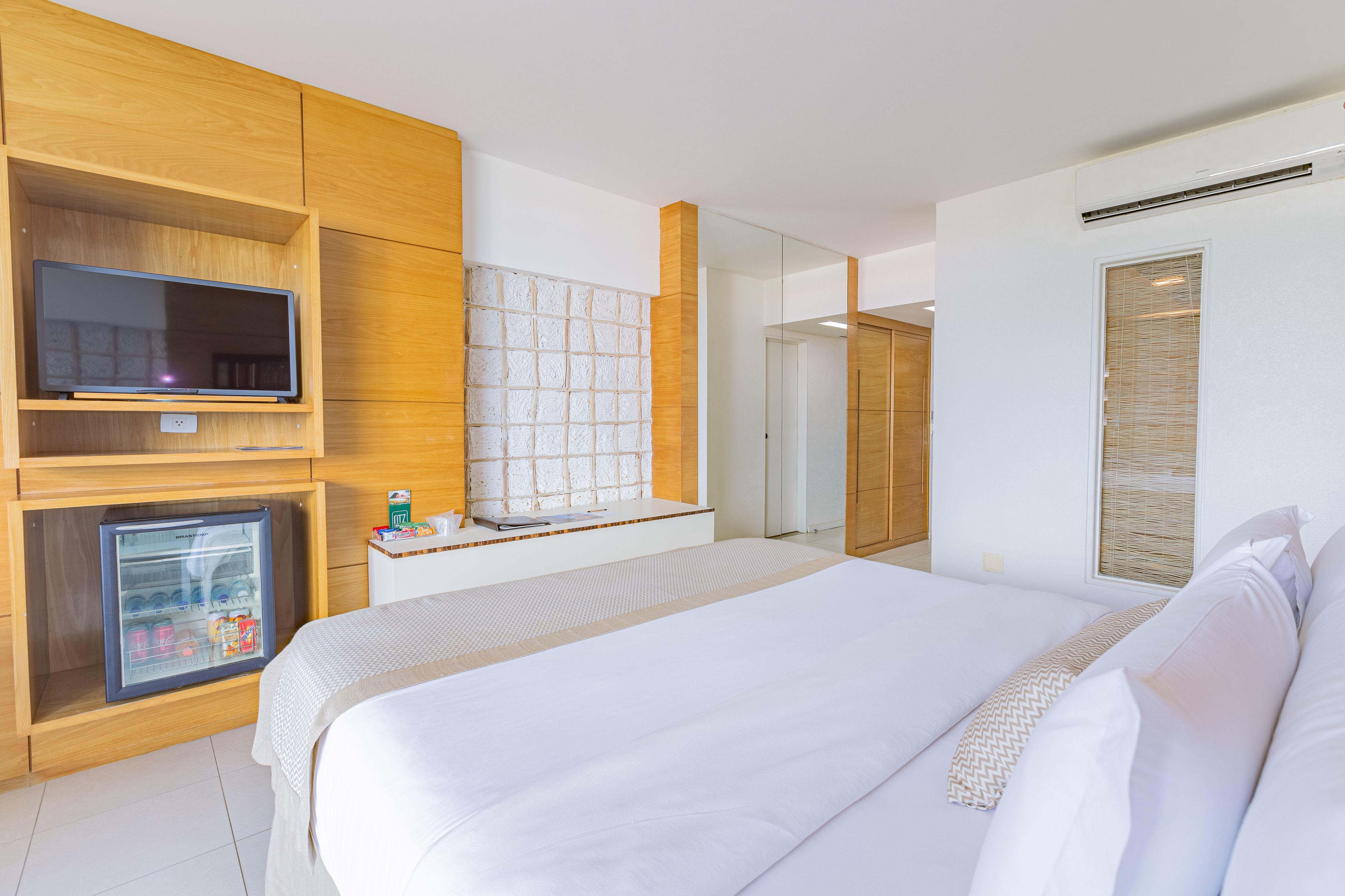 Una habitación de hotel con cama, televisor, minibar y espejo.