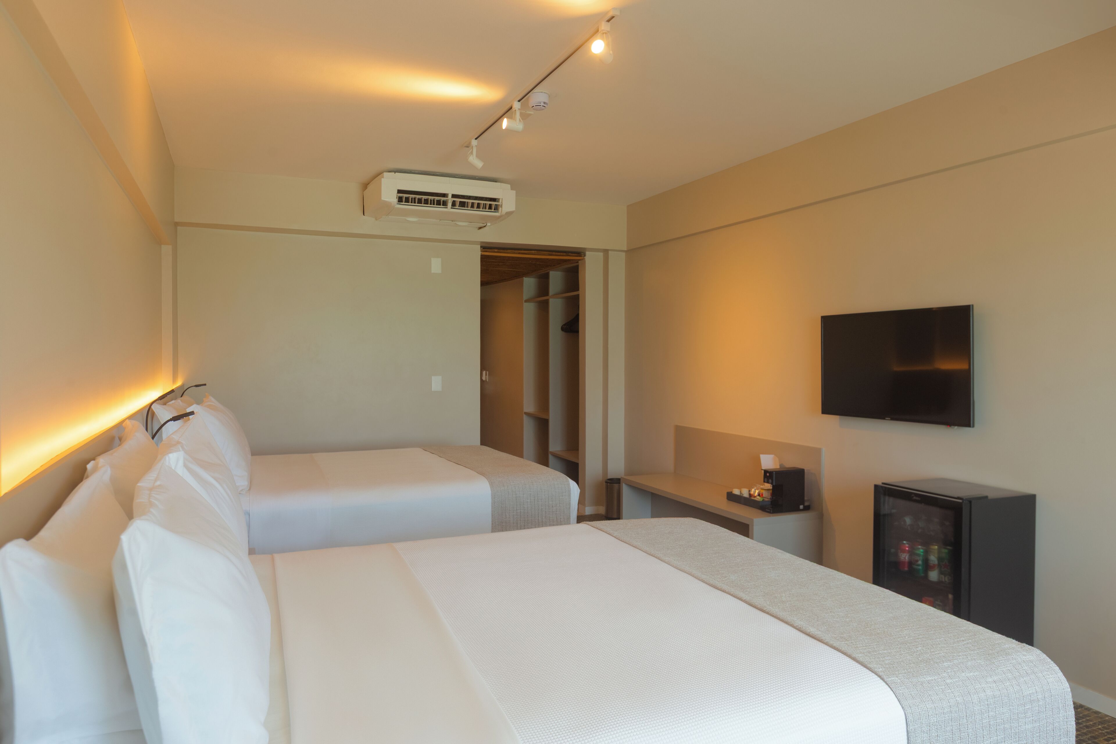 Quarto de hotel com duas camas, televisão, minibar e armário.