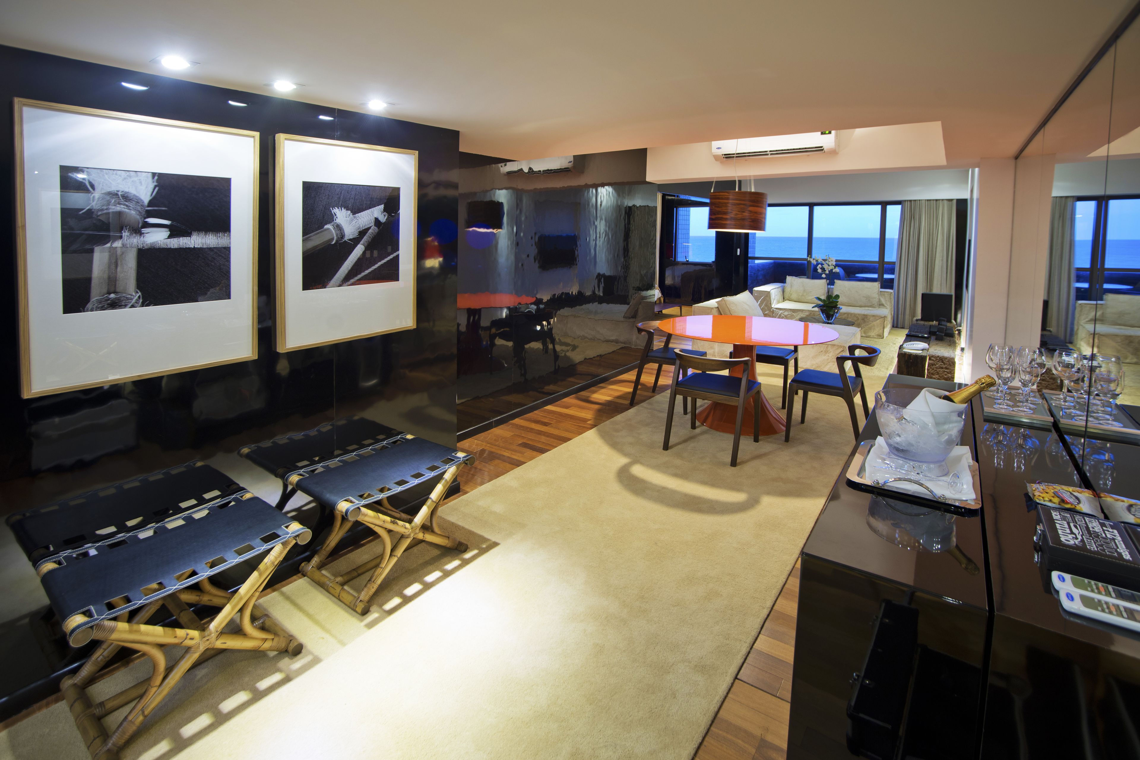A modern living room with a large window, a dining area, and a seating area with a view of the ocean.