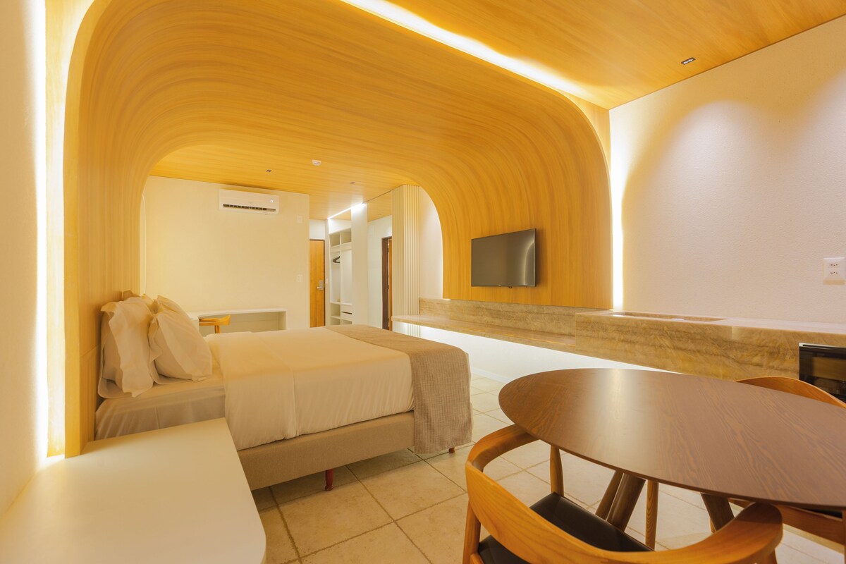 Habitación de hotel con cama, mesita de noche, una silla, televisor montado en la pared y techo de madera.