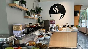 Et buffetområde med forskellige spisemuligheder, en kaffemaskine og en stor logo på væggen.