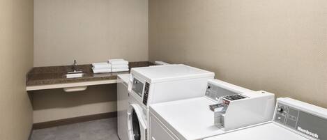 A laundry room with a washing machine, dryer, and a countertop with a sink and stacked towels.