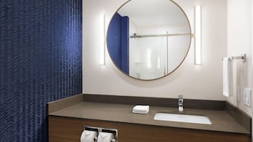 Ein Badezimmer mit einem Holzkosmetikschrank, einem runden Spiegel und einem Handtuchhalter.