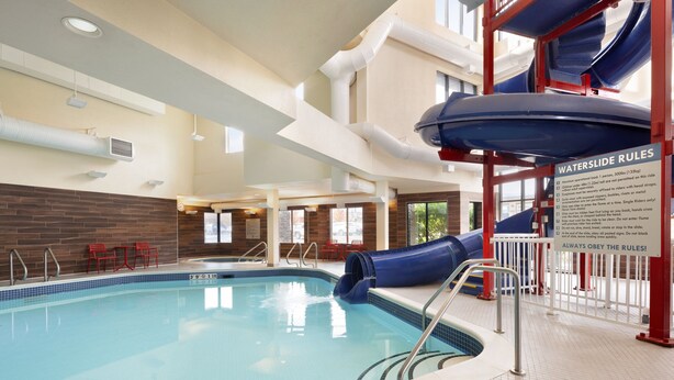An indoor swimming pool with a blue slide, a sign with water slide rules, and a tiled floor.