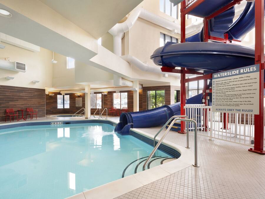 An indoor swimming pool with a blue slide, a sign with water slide rules, and a tiled floor.