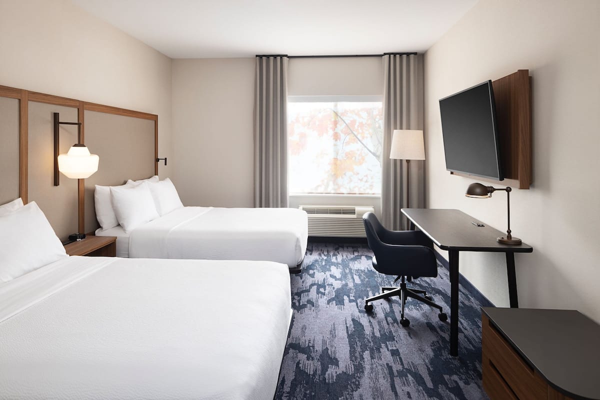 A hotel room with two beds, a desk, a chair, a TV, and a window with curtains.